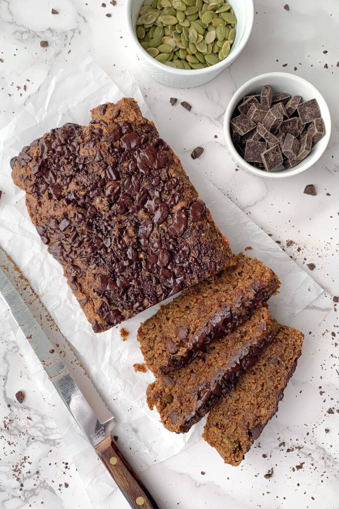 sliced breakfast loaf with knife, and bowls of pumpkin seeds and chocolate chunks