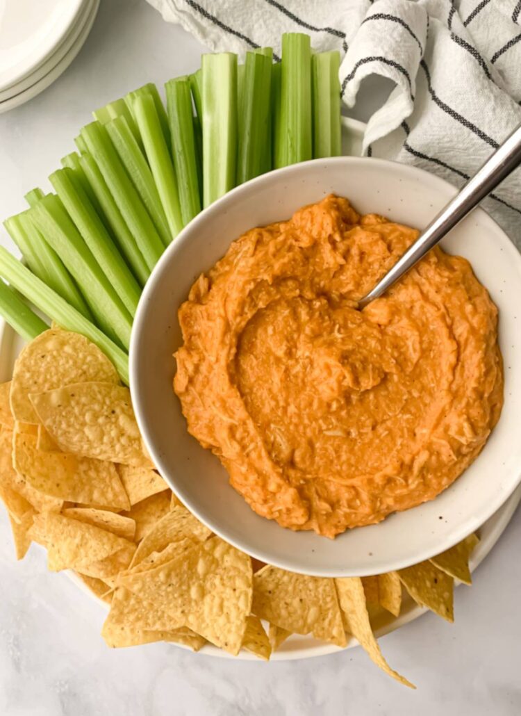 dairy free buffalo chicken dip in a bowl with spoon, surrounded by celery and tortilla chips.