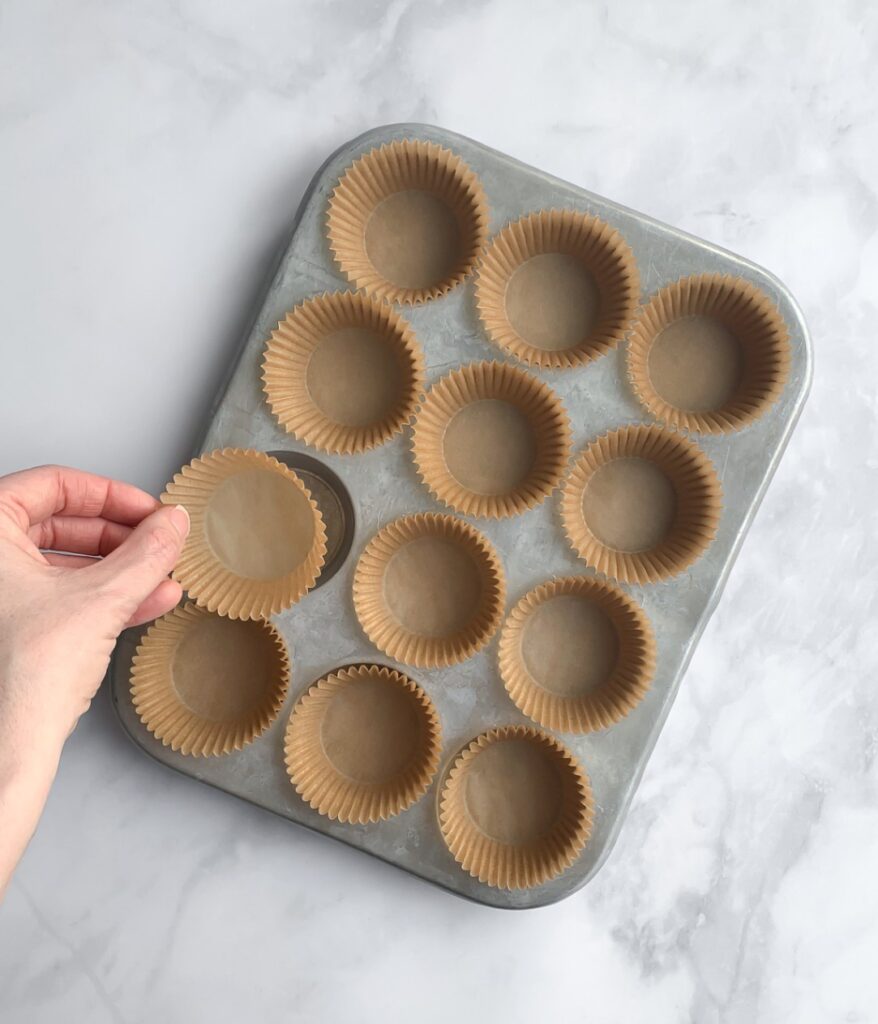 muffin liners being added to a muffin pan