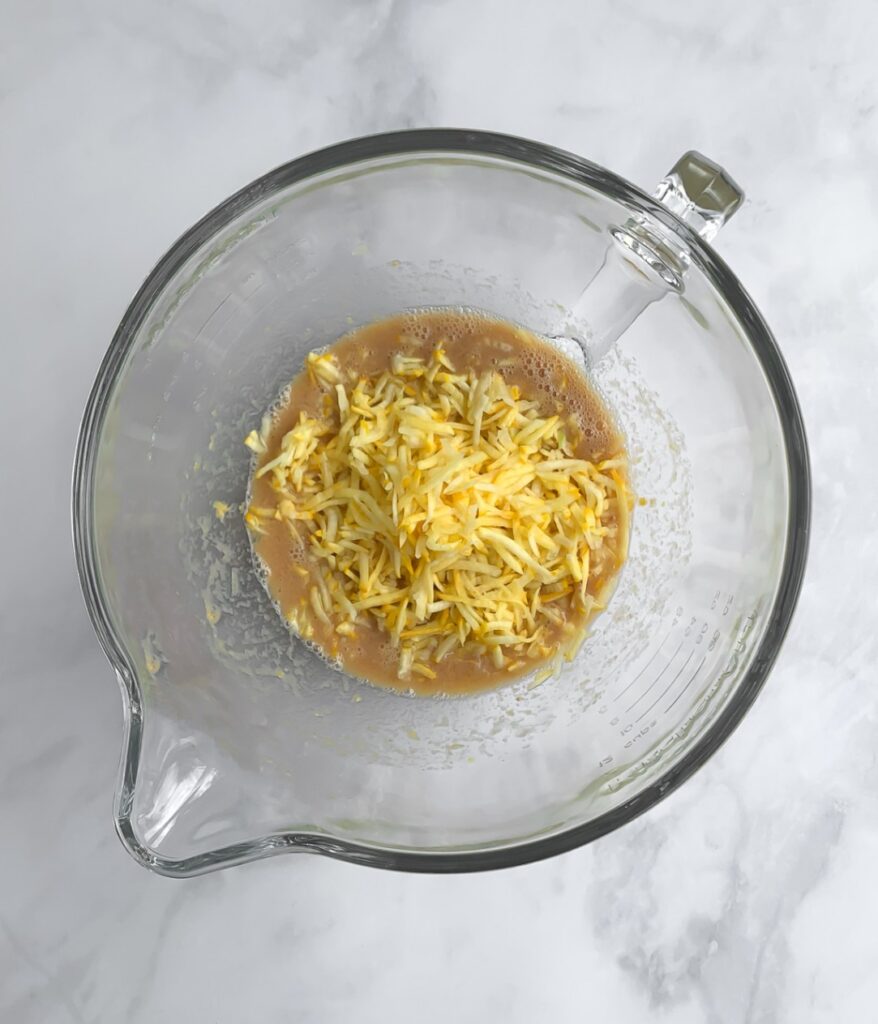 yellow zucchini being added to a bowl with wet ingredients