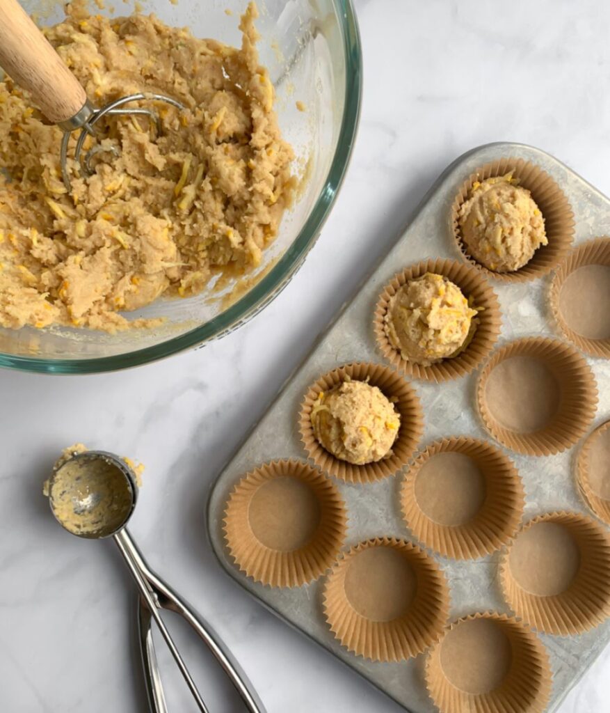 muffin batter being scooped into a muffin tin with an ice cream scoop.