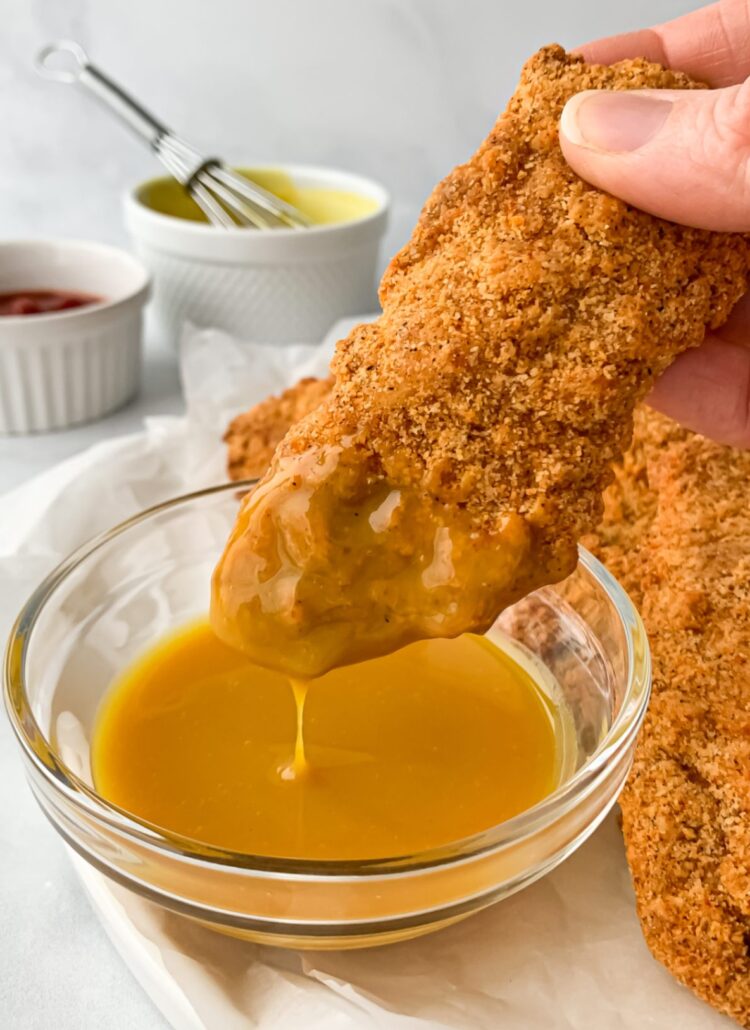 crispy chicken tender being dipped in honey mustard sauce