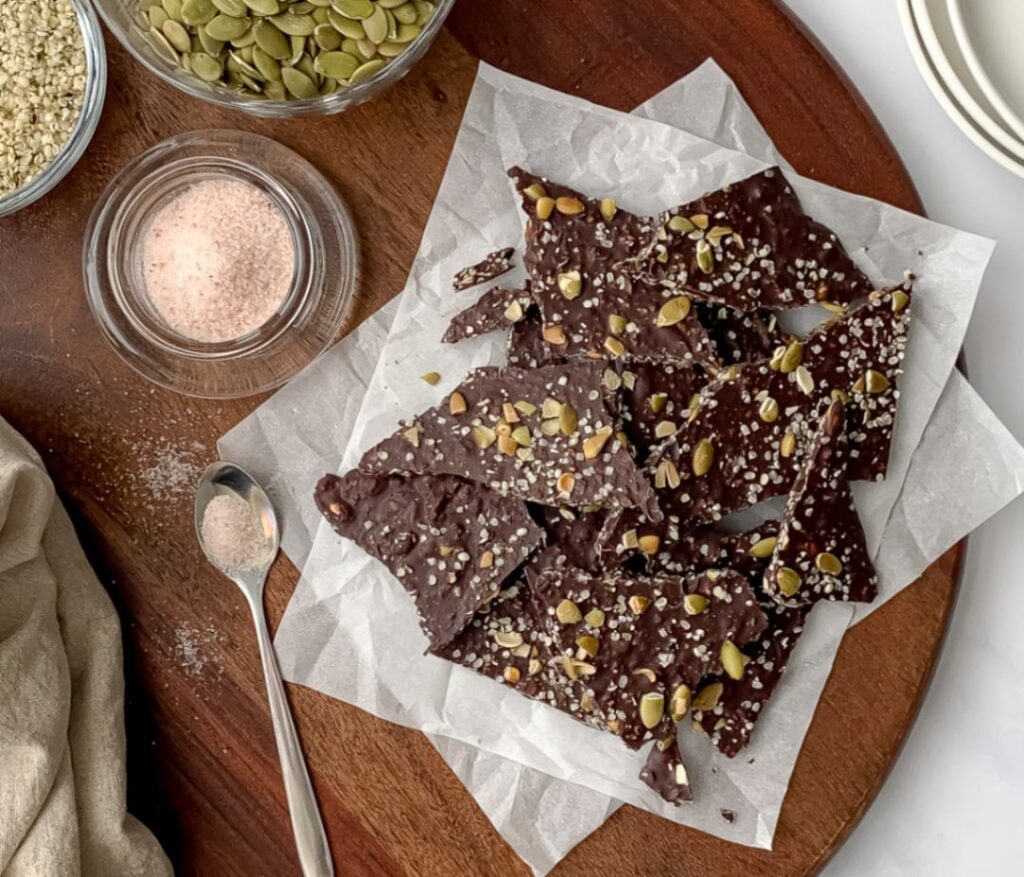 chocolate bark on a cutting board with pumpkin seeds and pink salt.