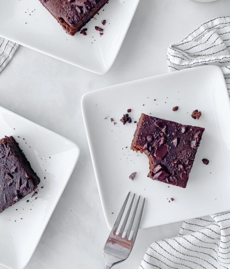 half eaten brownie on a small square plate with a fork.