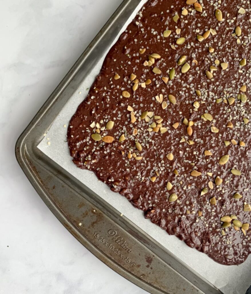 melted chocolate topped with seeds on a parchment lined baking pan