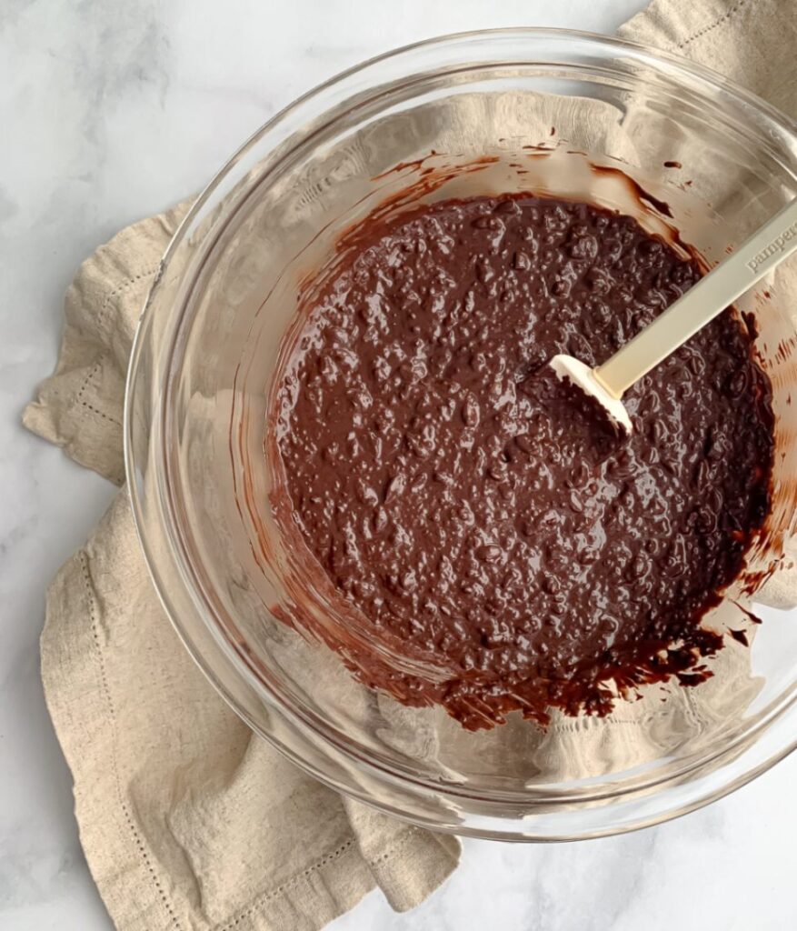 melted chocolate with seeds stirred in, in a glass bowl with a spatula