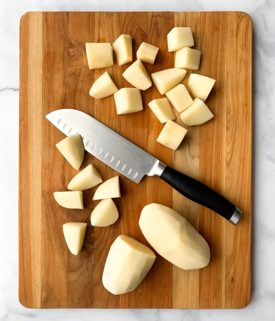 peeled potatoes being chopped on a wooden cutting board
