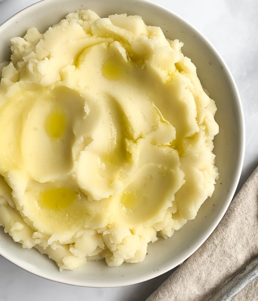 mashed potatoes in an off-white bowl garnished with olive oil