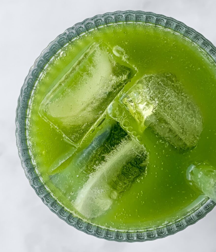 close up of matcha soda in a glass with ice.