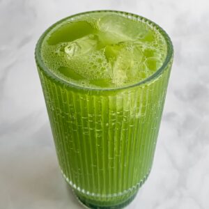 fizzing matcha soda in a tall ribbed glass with ice cubes.