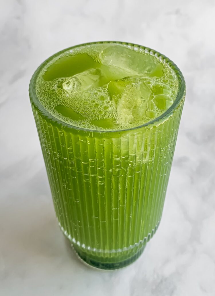 fizzing matcha soda in a tall ribbed glass with ice cubes.