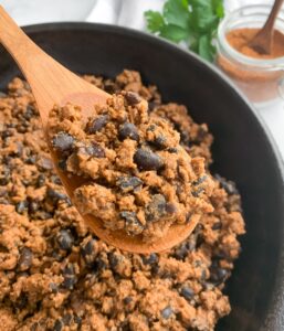 close up of taco meat with black beans on a wooden spoon