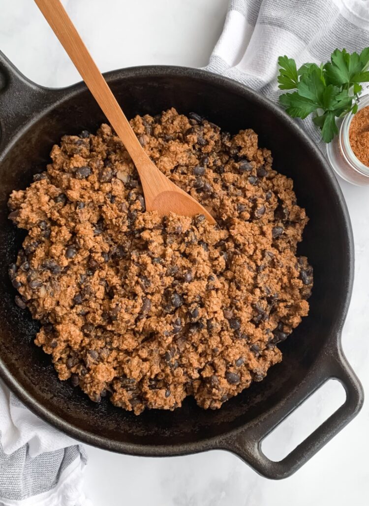 cast iron skillet with taco meat and black beans and a wooden spoon