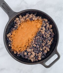 cast iron skillet with cooked ground beef, black beans and taco seasoning .