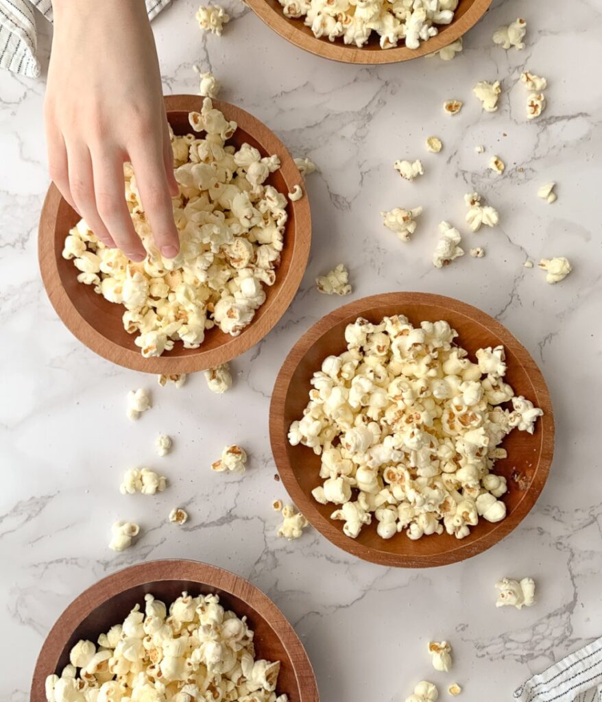 four wooden bowls with popcorn and a kid's hand taking popcorn from one of them