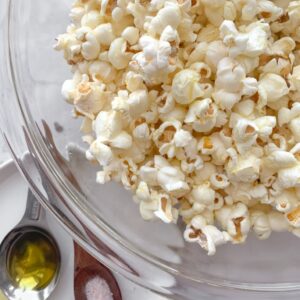 spoons on a white plate, each with olive oil and salt and popcorn in a glass bowl