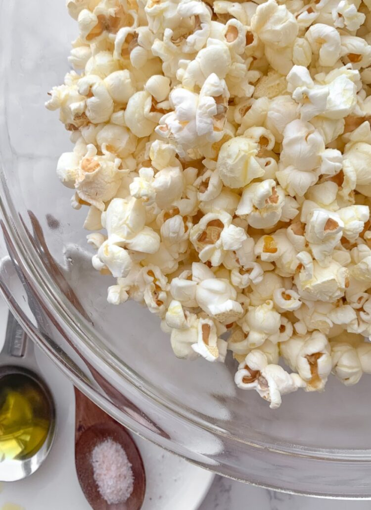 spoons on a white plate, each with olive oil and salt and popcorn in a glass bowl