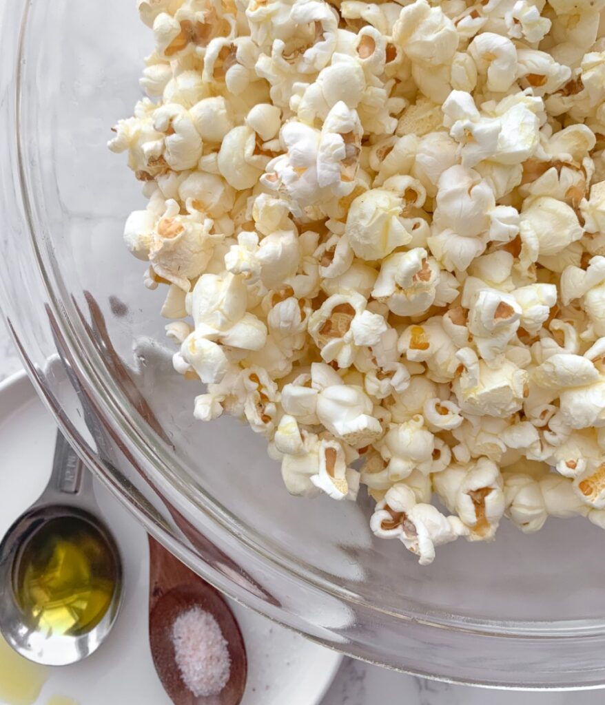 spoons on a white plate, each with olive oil and salt and popcorn in a glass bowl