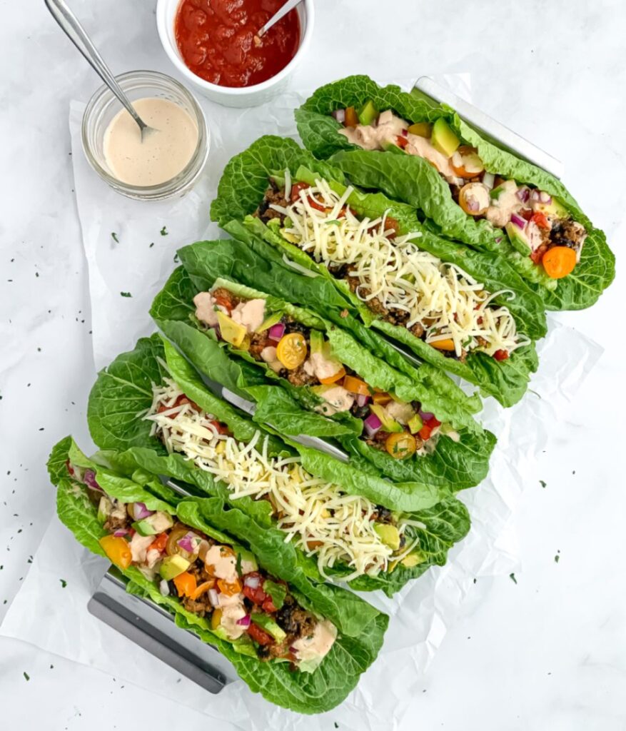 5 rainbow taco lettuce boats in taco holder with dairy free cheese sauce and salsa in small bowls to the side