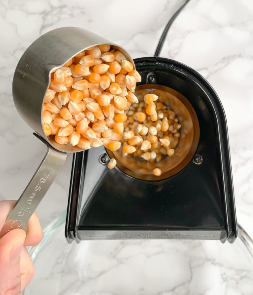 popcorn kernels being emptied from a measuring cup into an air popper machine