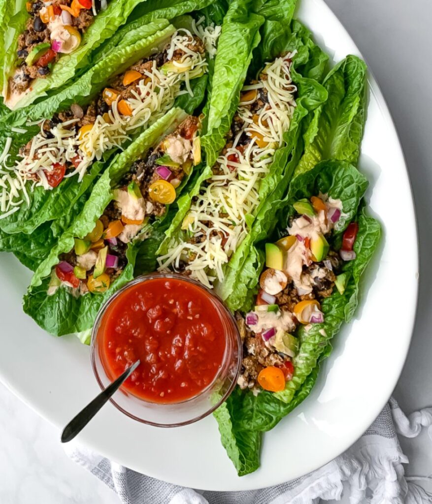 5 rainbow taco salad boats on a white plate with a small bowl of salsa