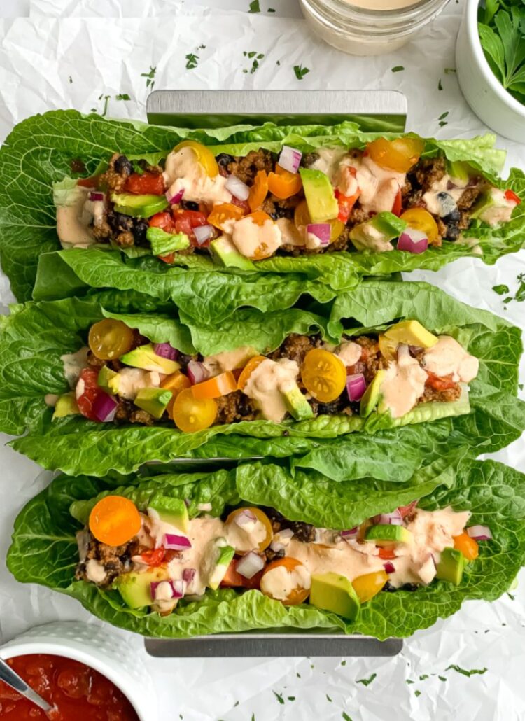 3 rainbow taco lettuce boats in taco holder with salsa, dairy free cheese sauce and cilantro in small bowls