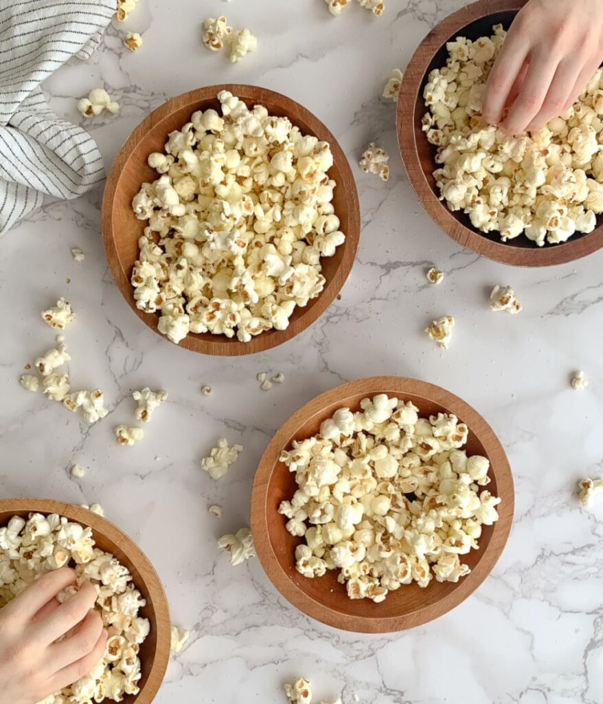 four wooden bowls with popcorn and two kids' hands taking popcorn from one of them