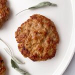 sausage patties on a white plate with dried sage leaves