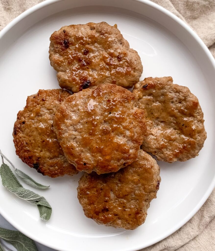 sausage patties stacked on a white plate with dried sage leaves