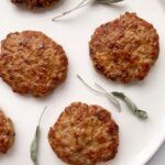 sausage patties on a white plate with dried sage leaves