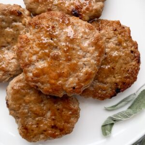 sausage patties stacked on a white plate with dried sage leaves