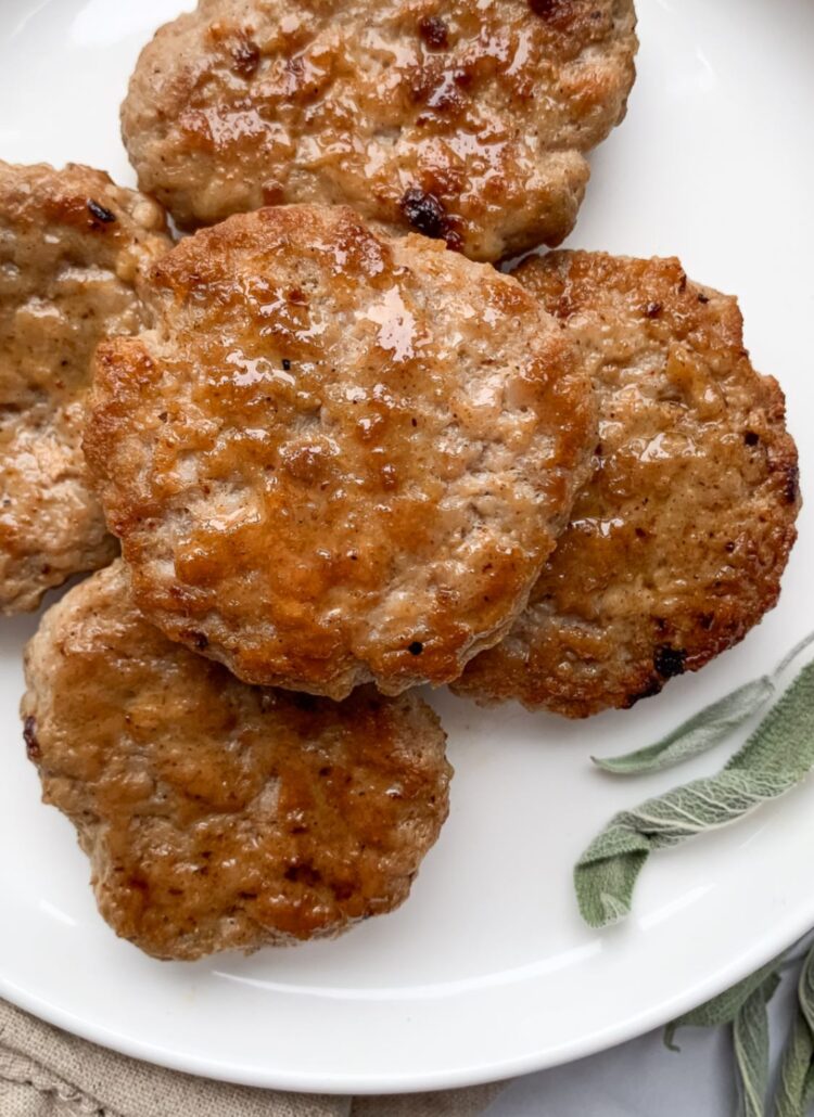 sausage patties stacked on a white plate with dried sage leaves