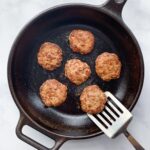 cooked chicken breakfast sausages on a cast iron skillet with a spatula lifting one