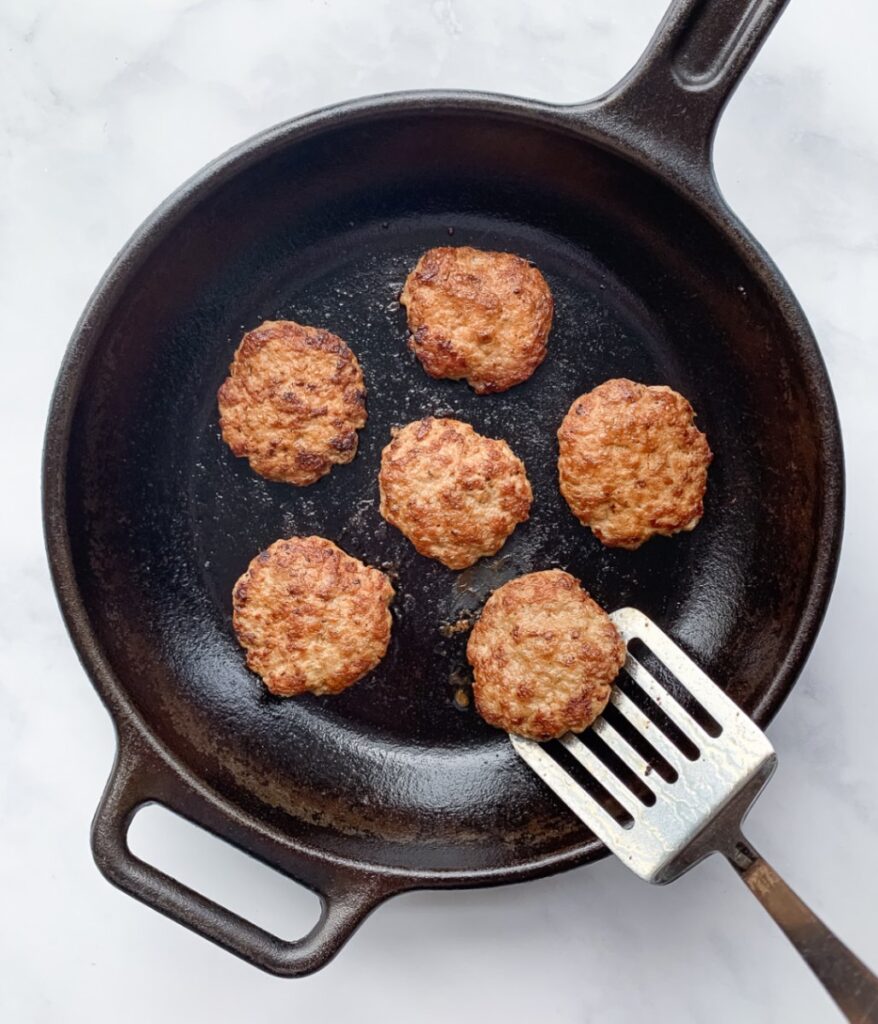 cooked chicken breakfast sausages on a cast iron skillet with a spatula lifting one