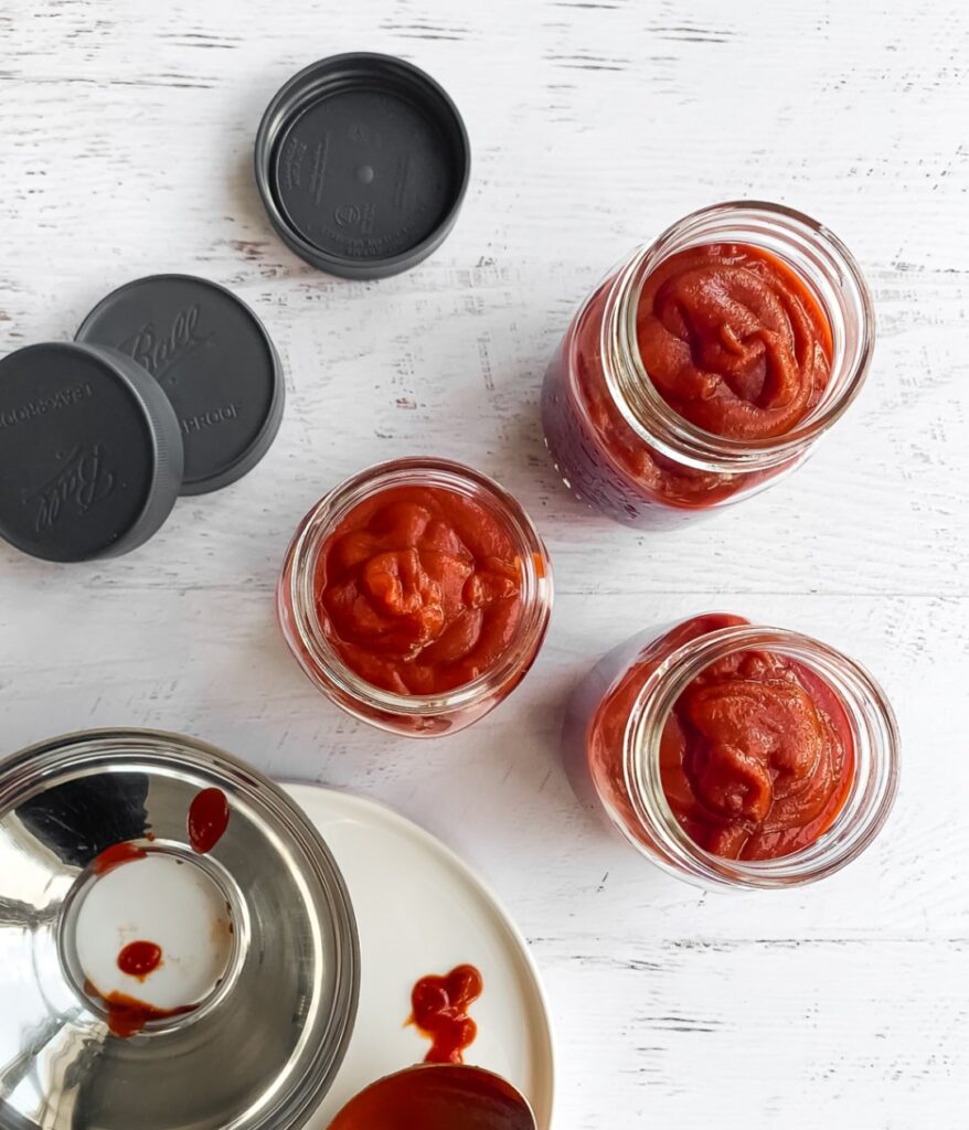 top down of 3 jars with ketchup with lids and funnel to the side