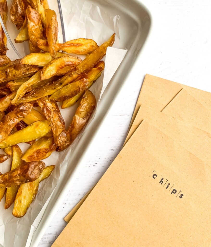 oven-baked potato wedges on a white baking dish with paper bags beside them, labelled 'chips'