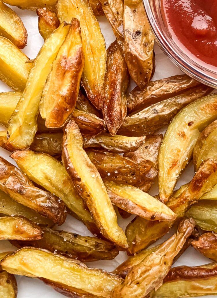 close up of crispy potato wedges on parchment paper with ketchup in a small bowl to the side