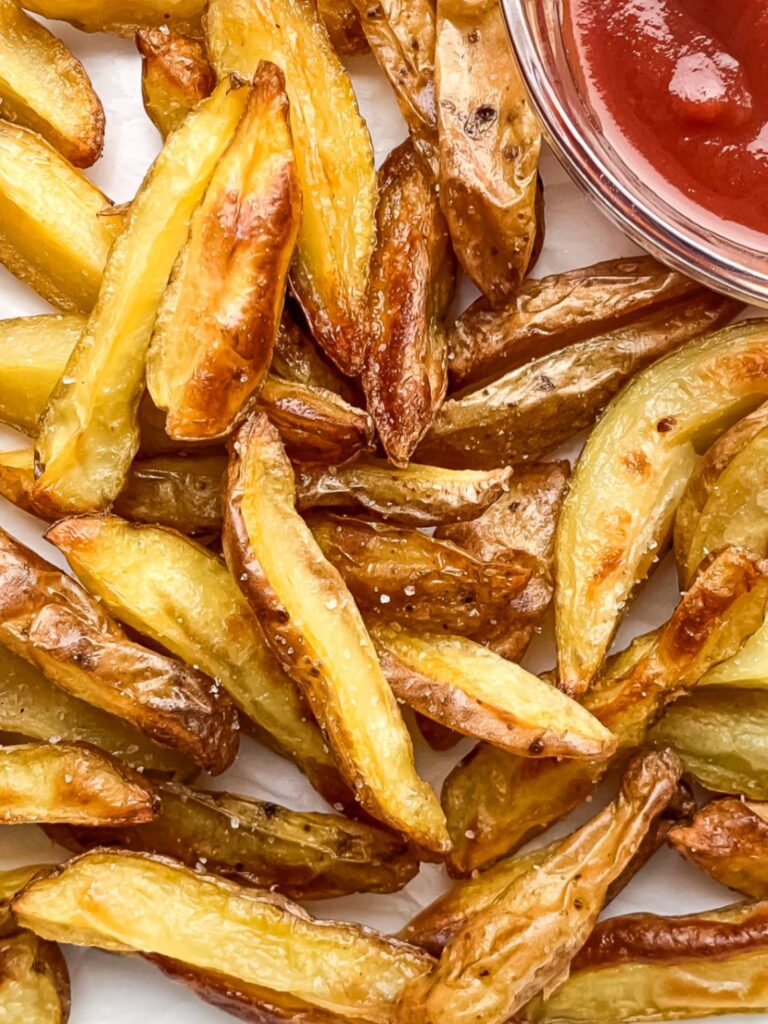 close up of crispy potato wedges on parchment paper with ketchup in a small bowl to the side