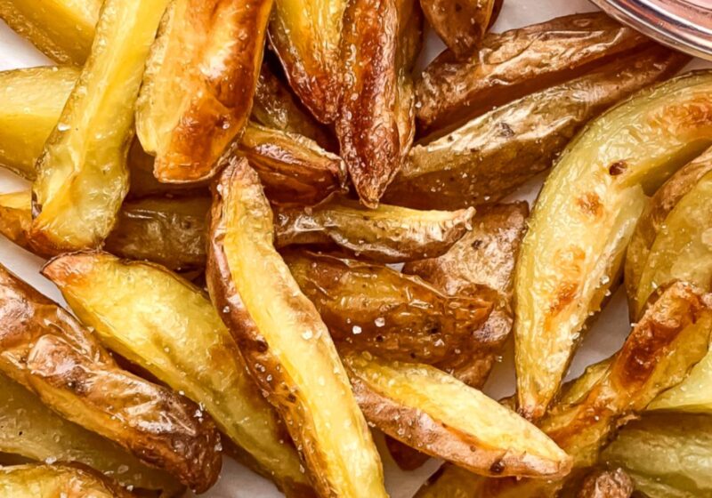 close up of crispy potato wedges on parchment paper with ketchup in a small bowl to the side