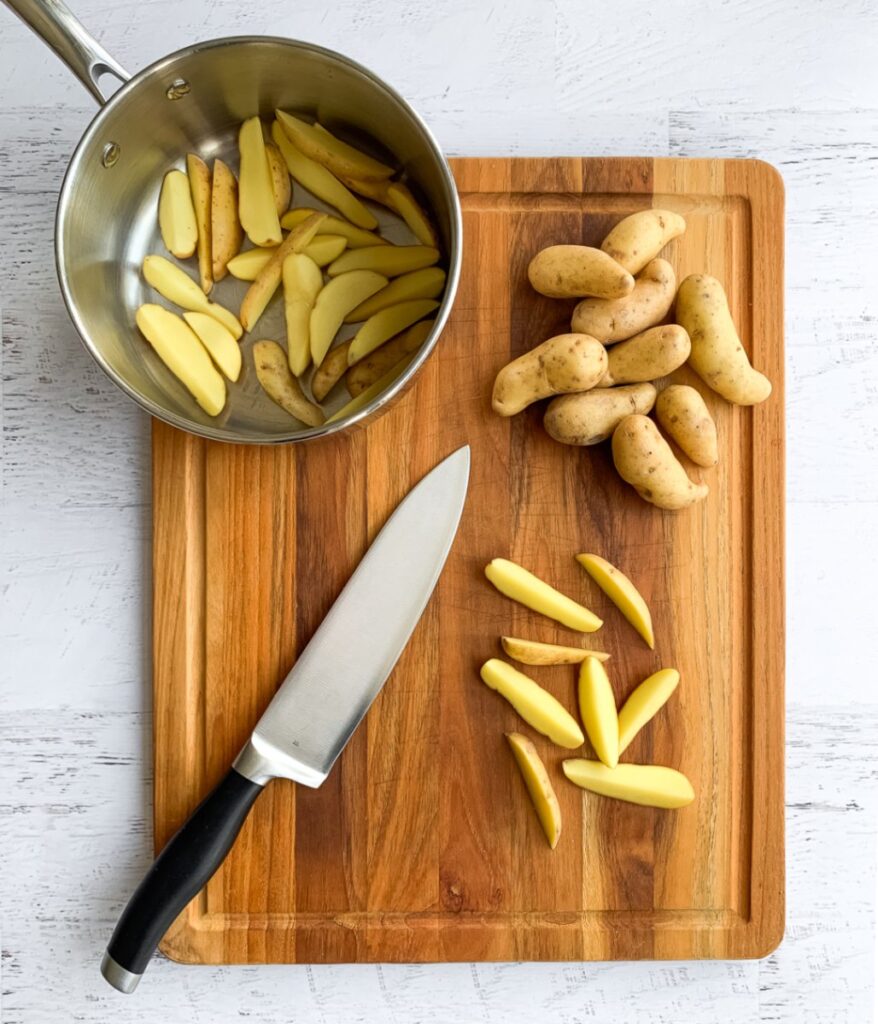 fingerling potatoes ibeing cut into wedges on a wooden cutting board