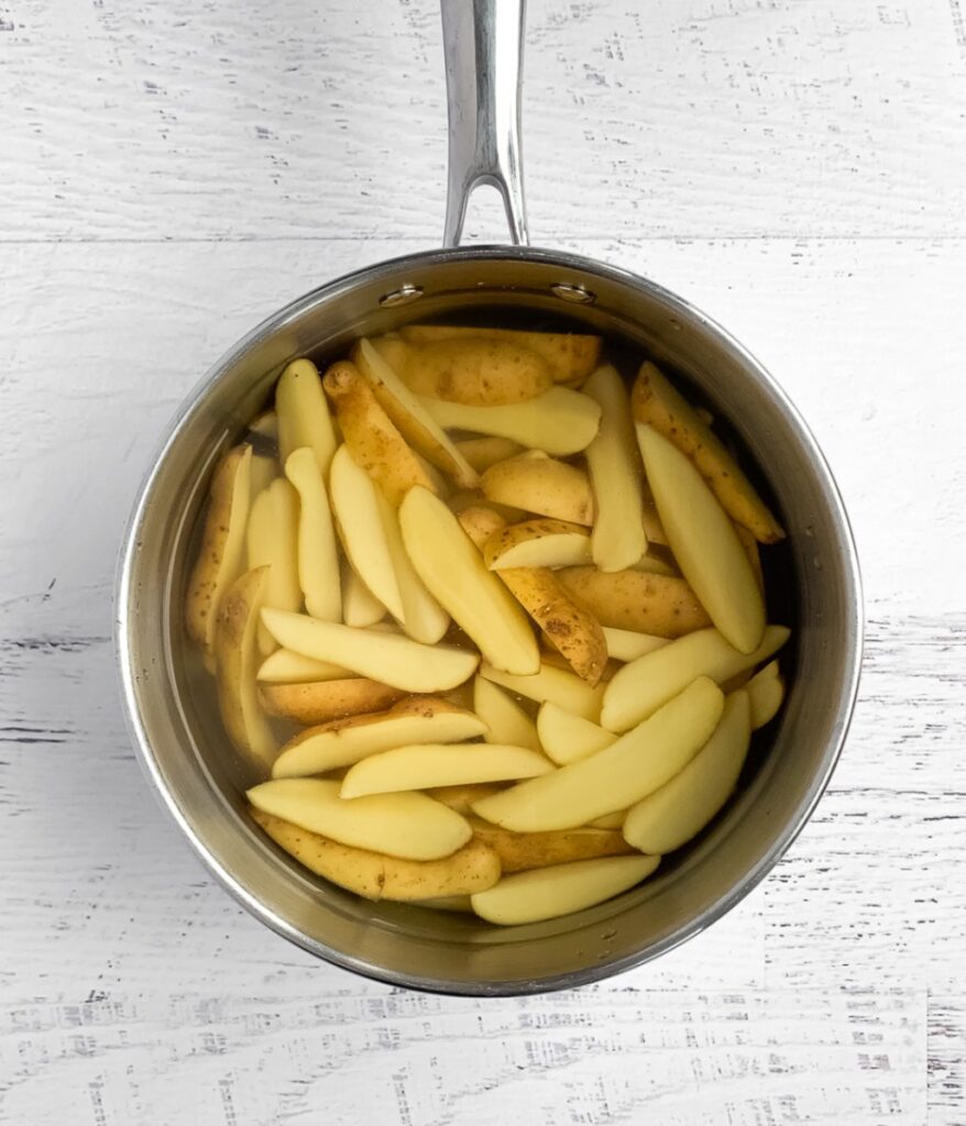 sliced raw potatoes in a pot covered in a water