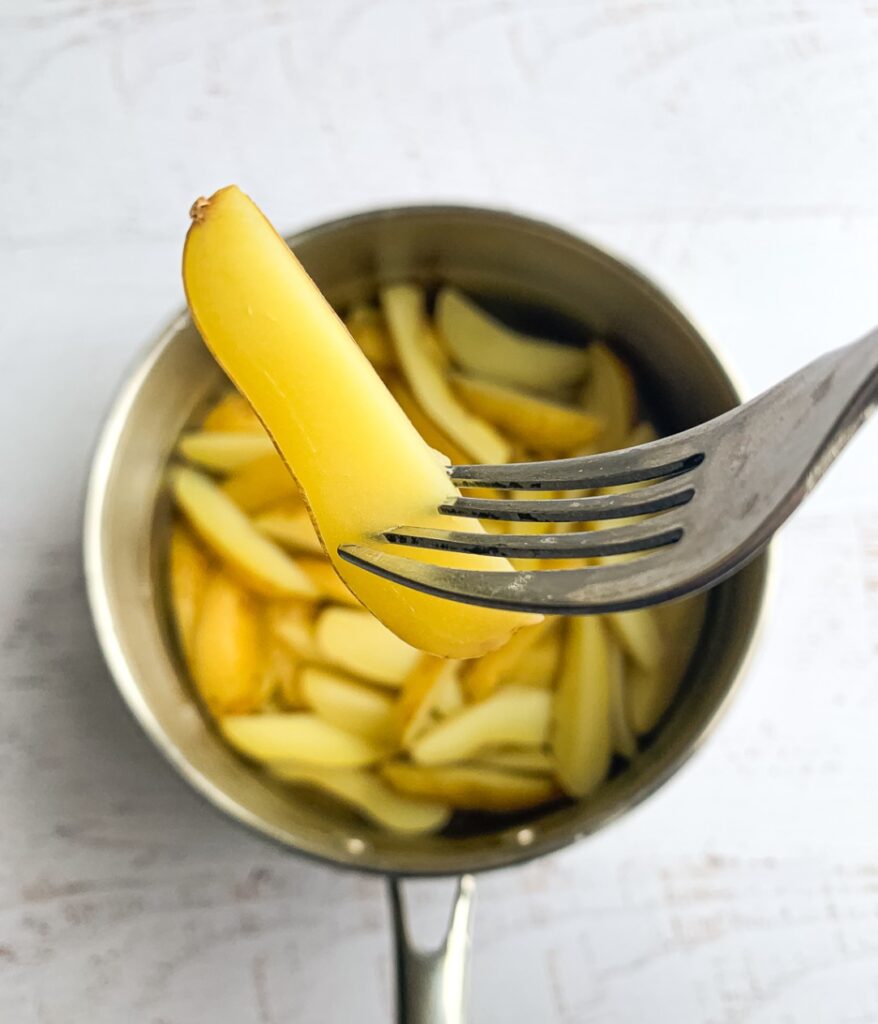 boiled potato wedges in a pot with one on a fork showing doneness