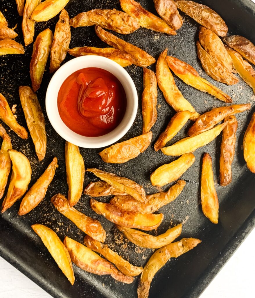 crispy potato wedges on a baking sheet with ketchup in a small bowl