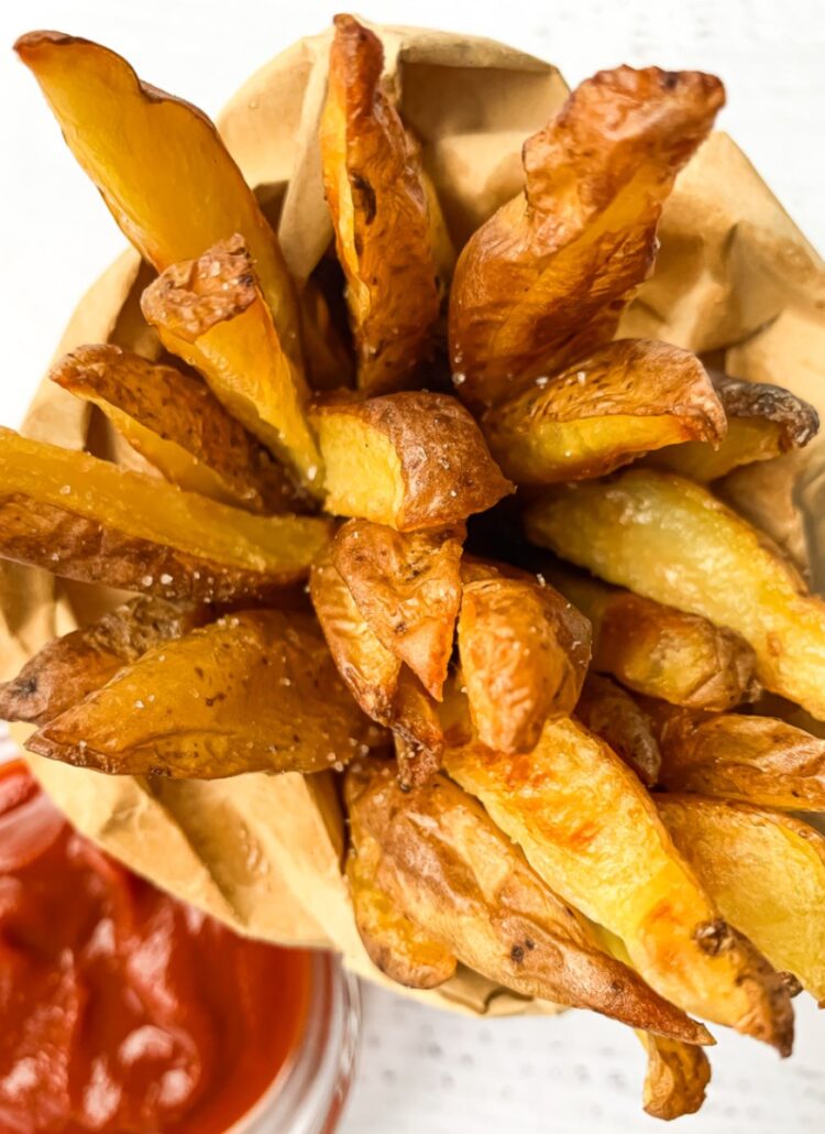 top down shot of potato wedge fries in a small brown paper bag with ketchup in a small bowl beside it