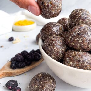 Hand holding a homemade blueberry energy ball above a bowl of no-bake energy bites