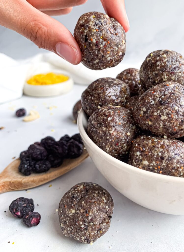 Hand holding a homemade blueberry energy ball above a bowl of no-bake energy bites