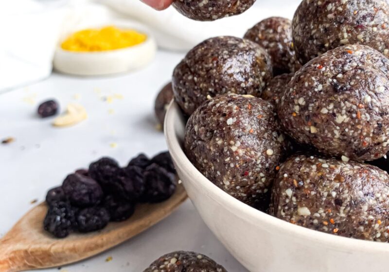 Hand holding a homemade blueberry energy ball above a bowl of no-bake energy bites