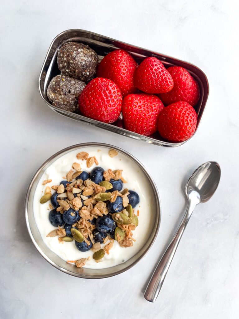 Healthy lunchbox with blueberry energy balls, strawberries and yogurt topped with granola