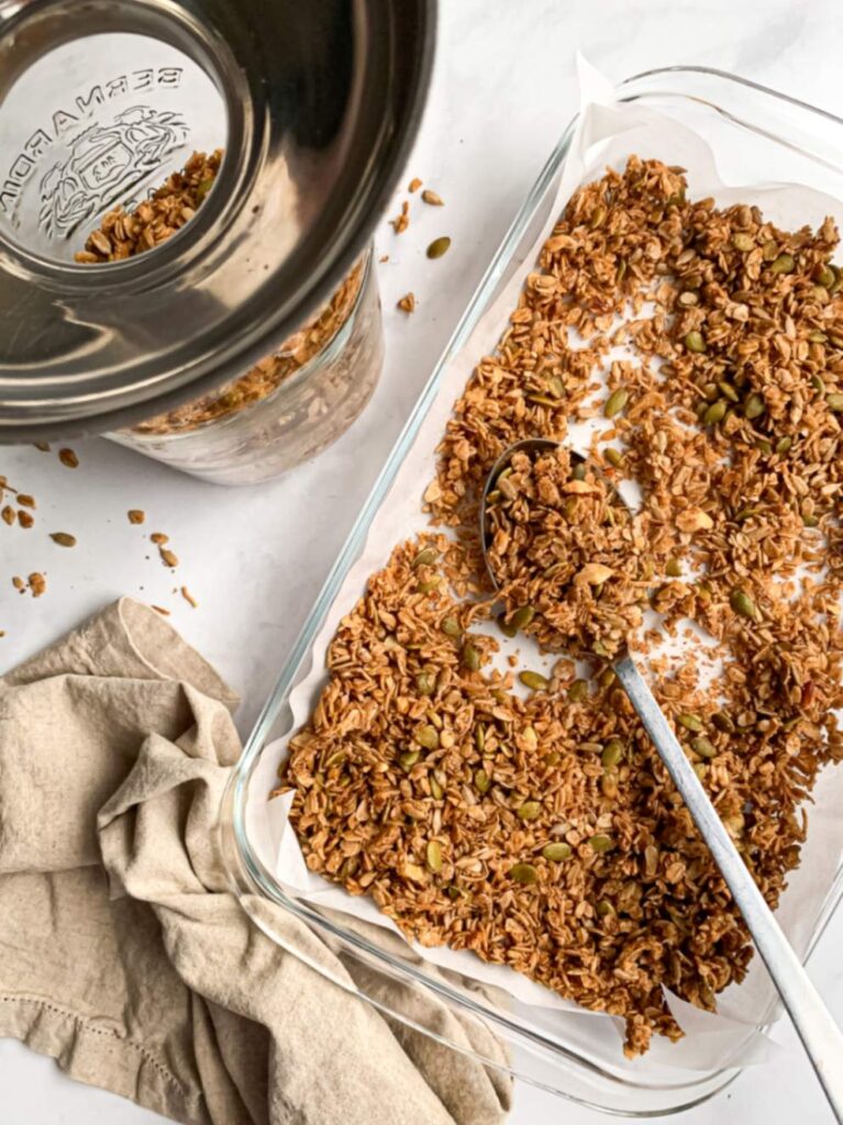 cooled granola in a prepared pan with large spoon with large mason jar with metal funnel to the side half full with the granola