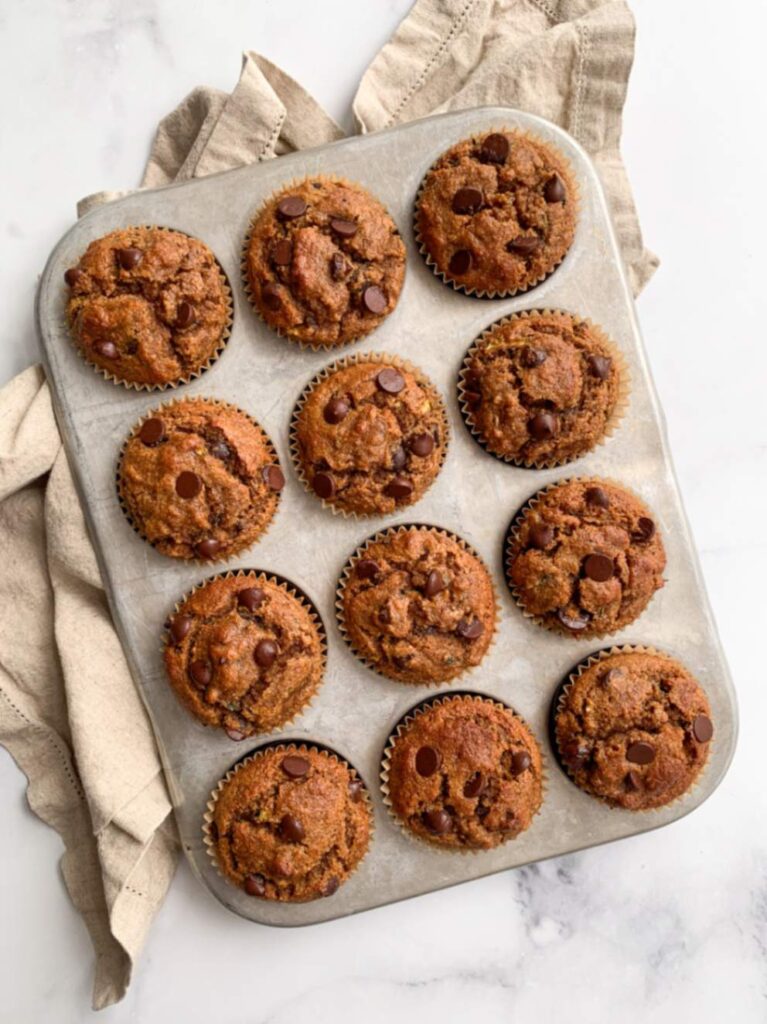 healthy chocolate chip zucchini muffins cooling in the muffin tin after baking with a tea towel.
